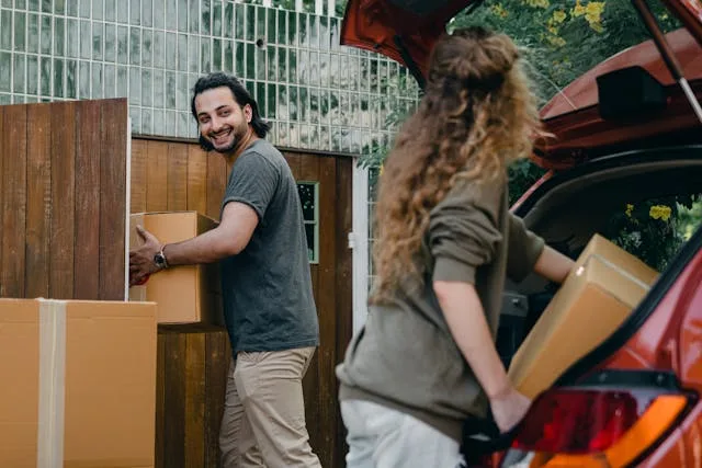  Two people carrying boxes into the house.